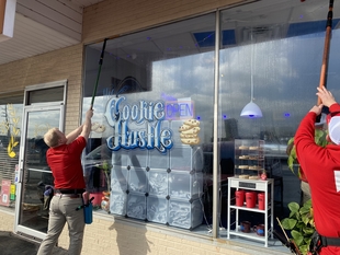 two window cleaners cleaning windows of a small coffee shop