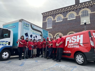 multiple fish window cleaners posing in front of a fish window cleaning van and a light blue and white mini semi truck
