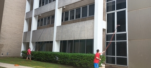 two window cleaners using poles to clean windows of a building