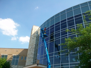 window cleaner cleaning windows of an all-glass building while on a lift