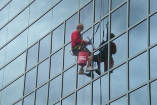 window cleaner hanging from suspenders while cleaning the side of an all-glass building
