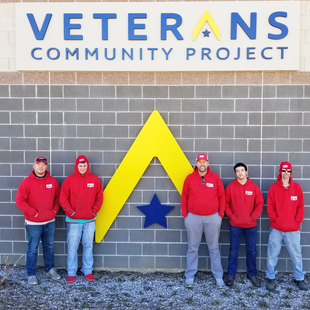 Fish Window Cleaning Team in Front of Veterans Community Project Logo on Wall