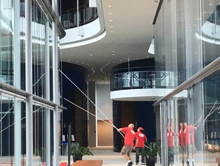Two FISH Window Cleaners Use Poles to Clean Walls of Glass in Lobby
