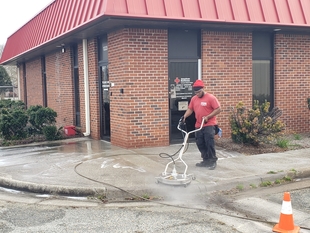 window cleaner pressure washing pavement in front of building
