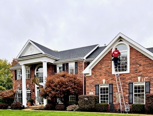 Large 2-Story Brick Home with Window Cleaner Cleaning 2nd Story Window on Ladder