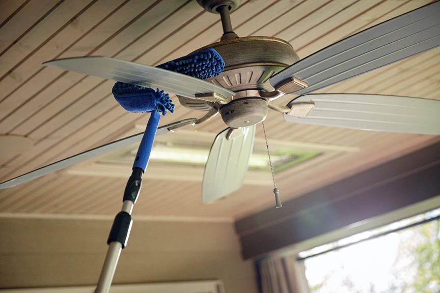 Celing fan being cleaned with a blue pad on a pole
