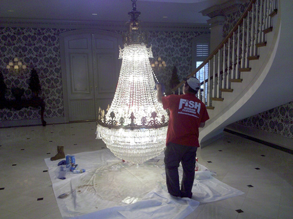 Person in red Fish Window Cleaning shirt and hat cleaning a chandelier.