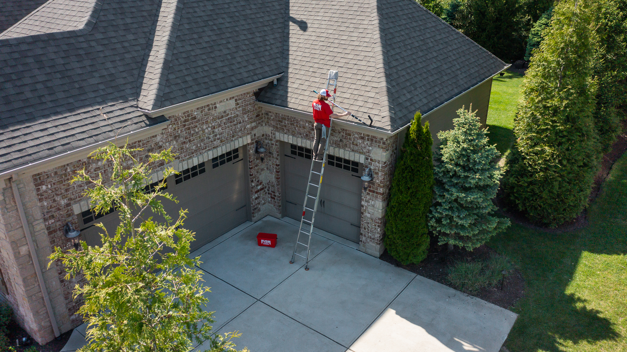 Aerial View of Cleaner Cleaning Gutters on a Ladder
