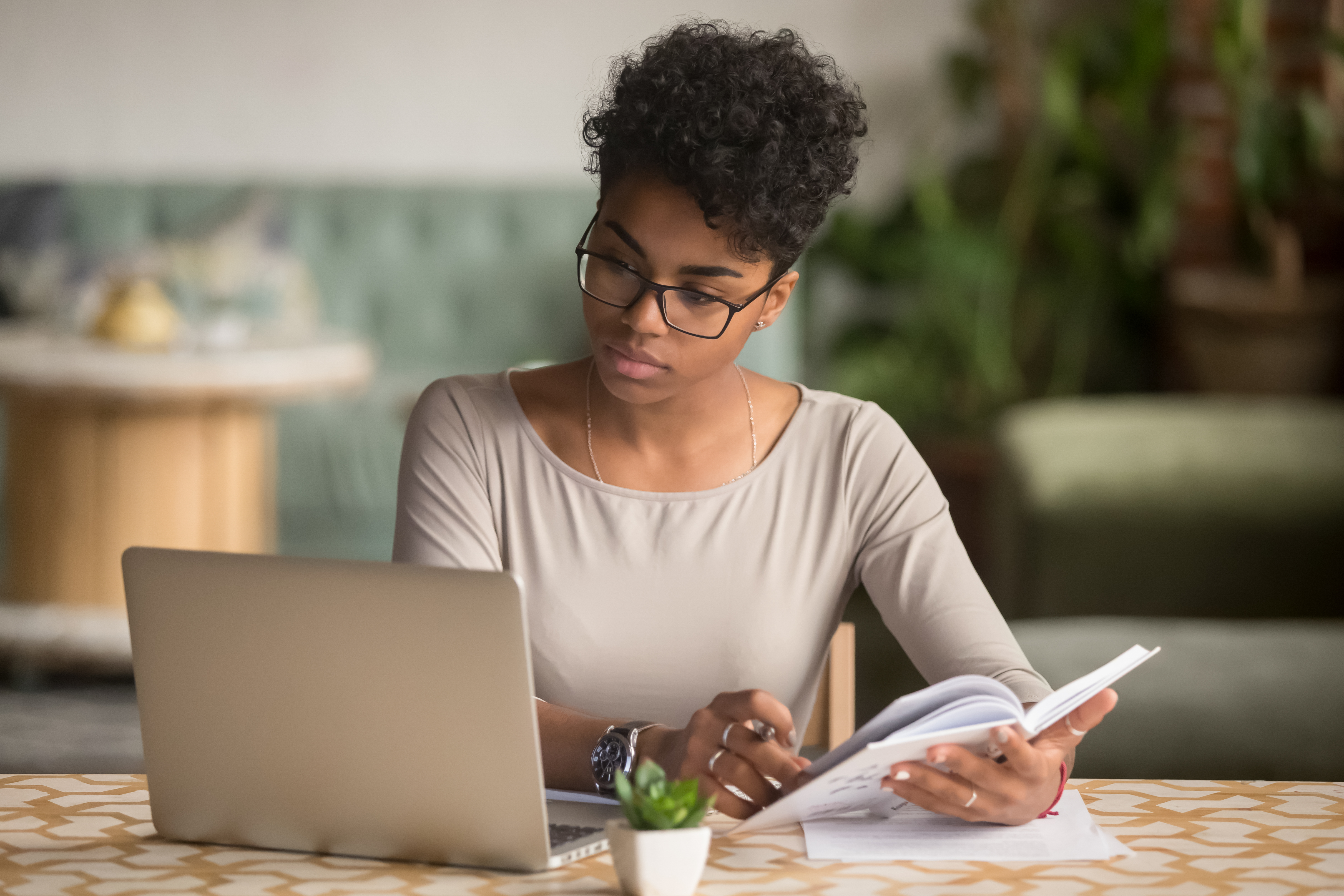 Young Woman Looking at Laptop Holding Book Doing Research