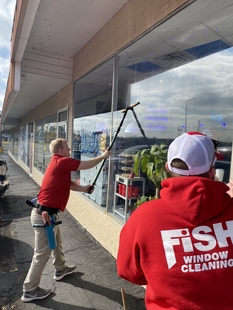 two window cleaners cleaning windows of a small coffee shop
